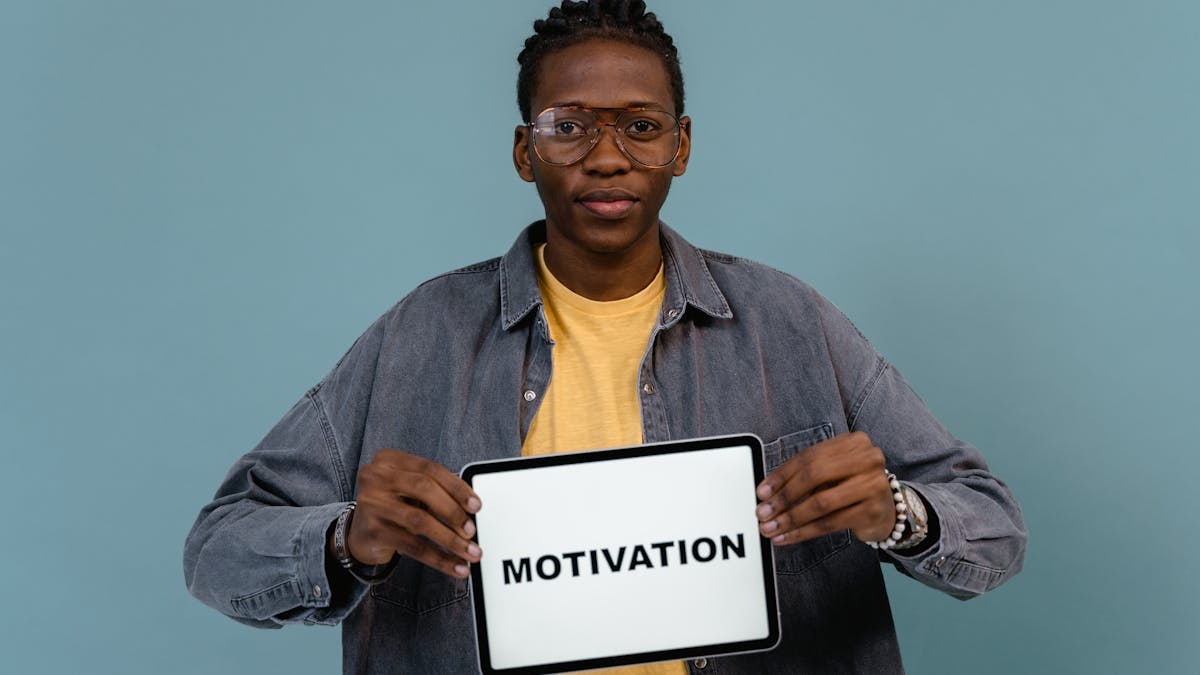 A young African American man holding a tablet displaying the word 'MOTIVATION' against a blue background.